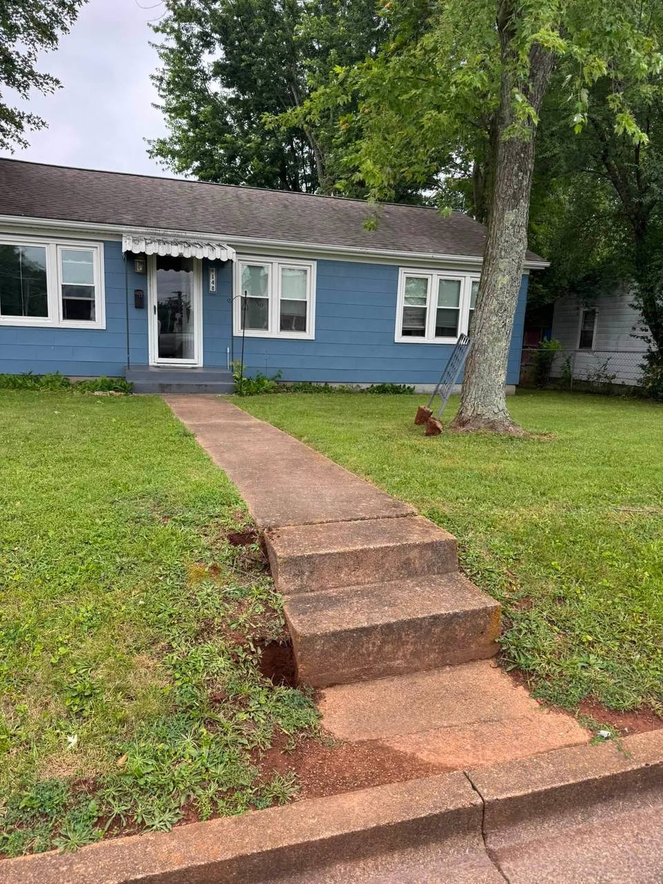 Old cracked front walk and worn steps at a blue house, before replacement